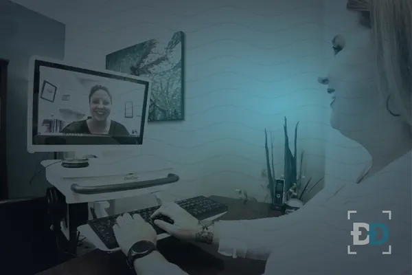 A smiling woman at a keyboard talks with a counselor who appears on a video call on a monitor.